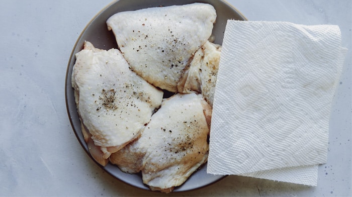 Chicken thighs being patted with paper towels.