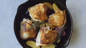 Crispy chicken thighs in a skillet with potatoes.