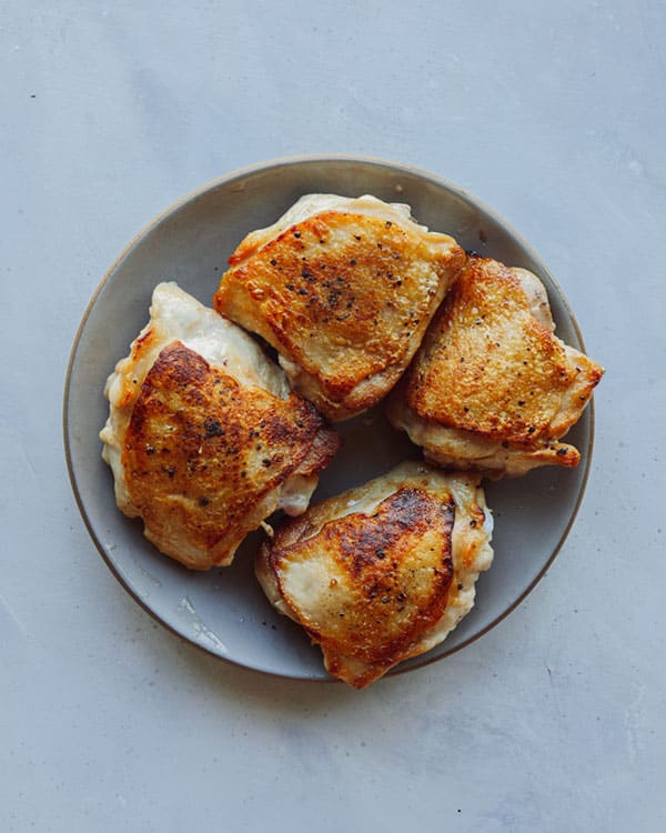 Cooked chicken thighs resting on a plate.