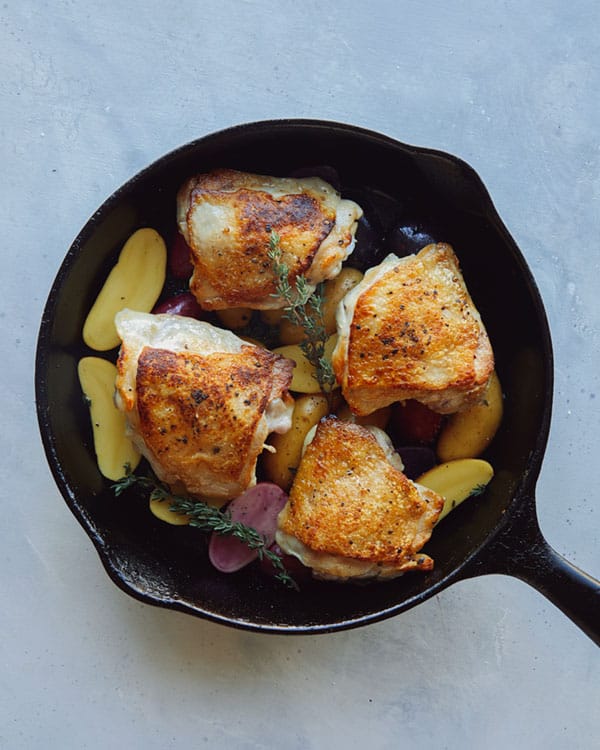 Crispy chicken thighs in a skillet with potatoes.