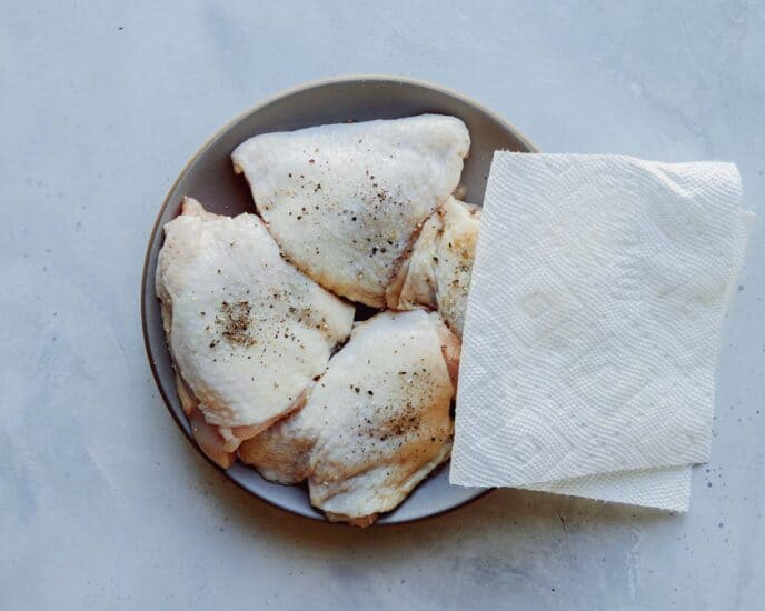 Chicken thighs being patted with paper towels. 