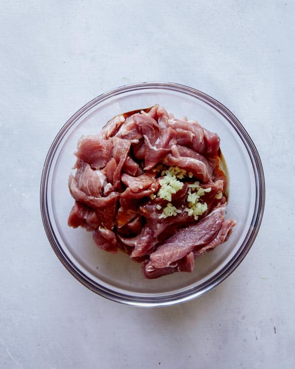 Pork ingredients in a glass bowl for pad see ew.