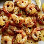 Shrimp scampi recipe on a plate with lemon wedges.