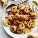 Shrimp scampi recipe on a plate with lemon wedges.