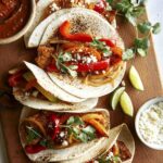 Chicken fajitas in tortillas on a board.