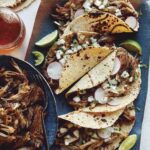 Easy carnitas recipe in a bowl next to a plate of tacos.