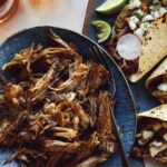 Carnitas being served with tacos and beer.