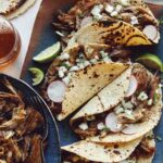 Easy carnitas recipe in a bowl next to a plate of tacos.