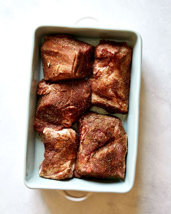 Pork shoulder rubbed with spices in a baking dish.