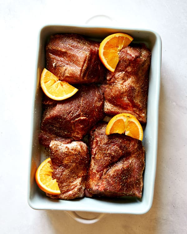 Pork shoulder in a baking dish with orange wedges to make carnitas. 