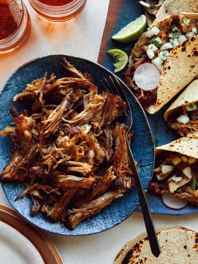 Carnitas being served with tacos and beer. 