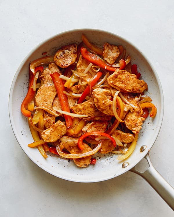Chicken fajitas in skillet cooking.