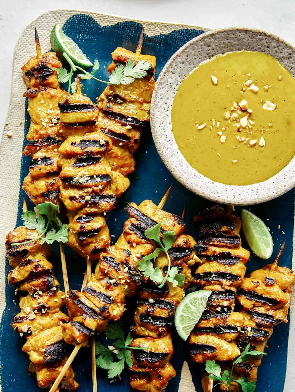 Chicken satay on a platter with lime wedges.