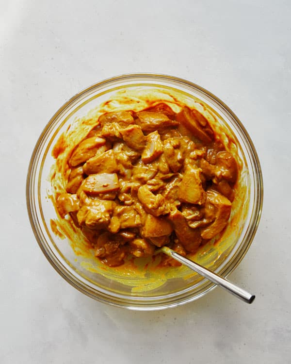 Chicken marinating in a glass bowl.