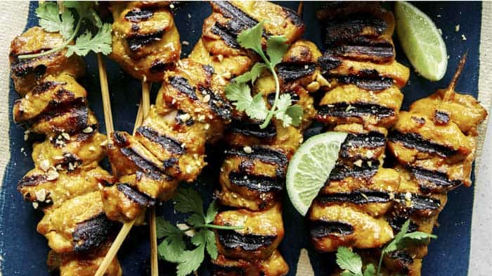 Chicken satay on a platter with lime wedges.