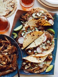 Easy carnitas recipe in a bowl next to a plate of tacos.