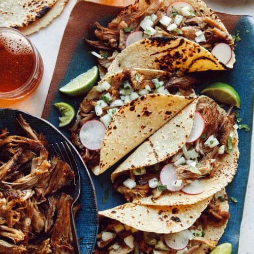 Easy carnitas recipe in a bowl next to a plate of tacos.