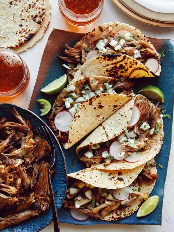 Easy carnitas recipe in a bowl next to a plate of tacos. 