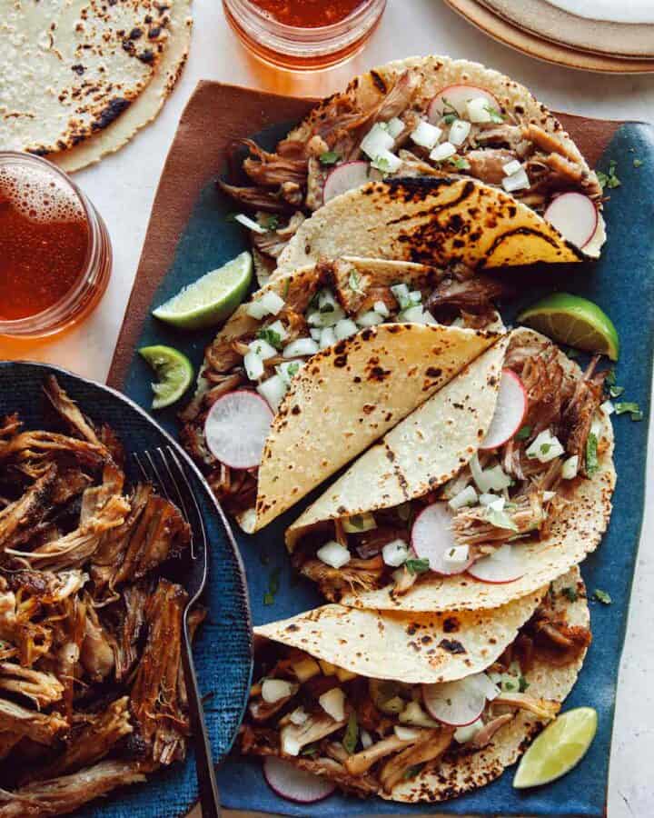 Easy carnitas recipe in a bowl next to a plate of tacos.