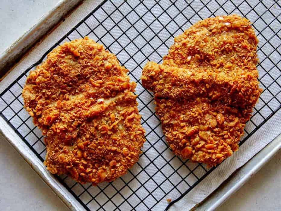 Freshly fried pork tenderloin cutlets on a baking sheet.