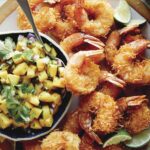 Coconut shrimp on a platter with a bowl of mango salsa.