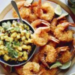 Coconut shrimp on a platter with a bowl of mango salsa.