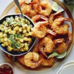 Coconut shrimp on a platter with a bowl of mango salsa.