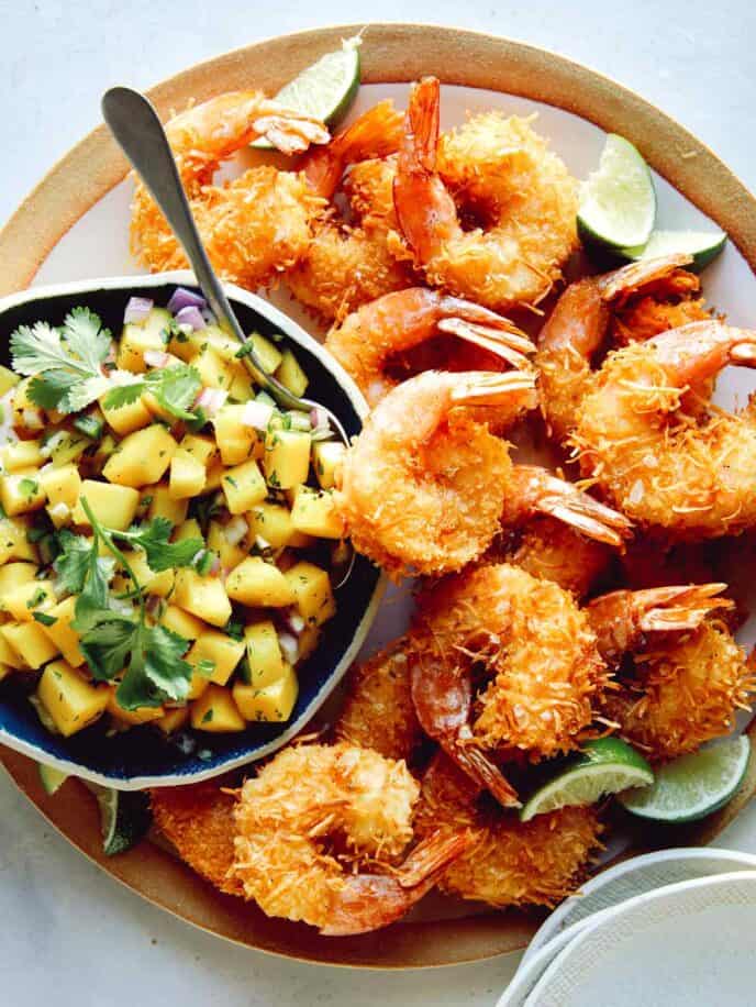 Coconut shrimp on a platter with a bowl of mango salsa.