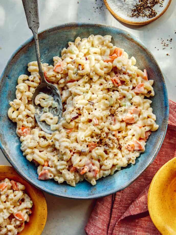 Hawaiian style macaroni salad in a bowl with serving bowls nearby.