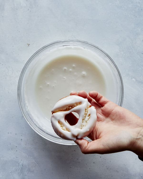 Dipping old fashioned donuts into a vanilla glaze.