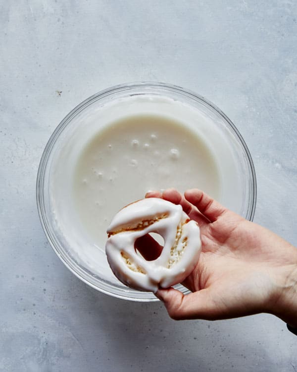 Dipping old fashioned donuts into  a vanilla glaze. 