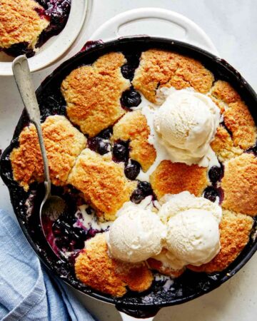 Blueberry cobbler recipe in a skillet with ice cream on top.