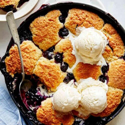 Blueberry cobbler recipe in a skillet with ice cream on top.