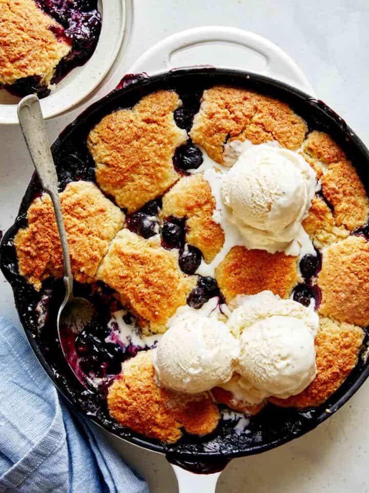 Blueberry cobbler recipe in a skillet with ice cream on top.