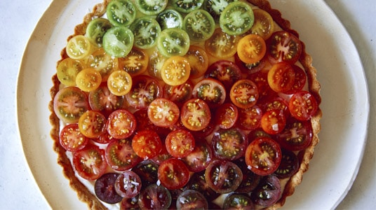 Tomato tart recipe on a platter with fresh tomatoes on the side.