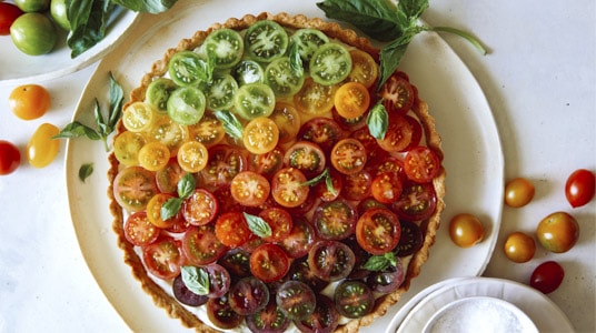Tomato tart on a platter with white wine in the background.