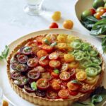 Tomato tart on a platter with white wine in the background.