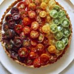 Tomato tart recipe on a platter with fresh tomatoes on the side.