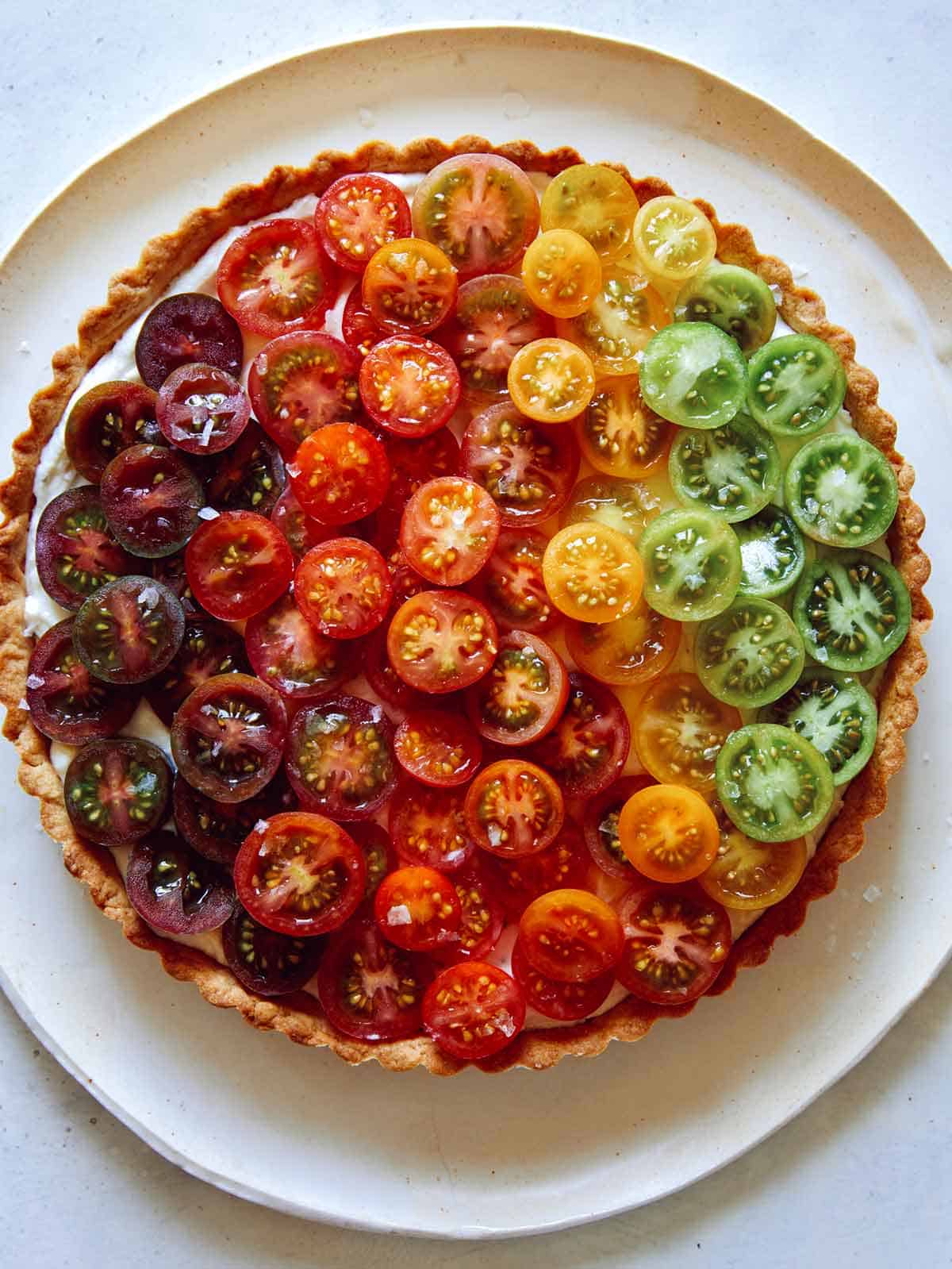 Close up on an ombre tomato tart with different colors of tomatoes.
