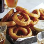 Beer battered fried onion rings with ranch dressing and beer on the side.