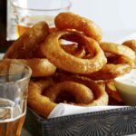 Beer battered fried onion rings with ranch dressing and beer on the side.