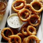 A serving of beer battered fried onion rings with ranch.