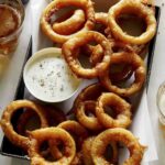 Beer battered fried onion rings with beer next to it.