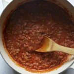Bolognese sauce in a stock pot with a wooden spoon.