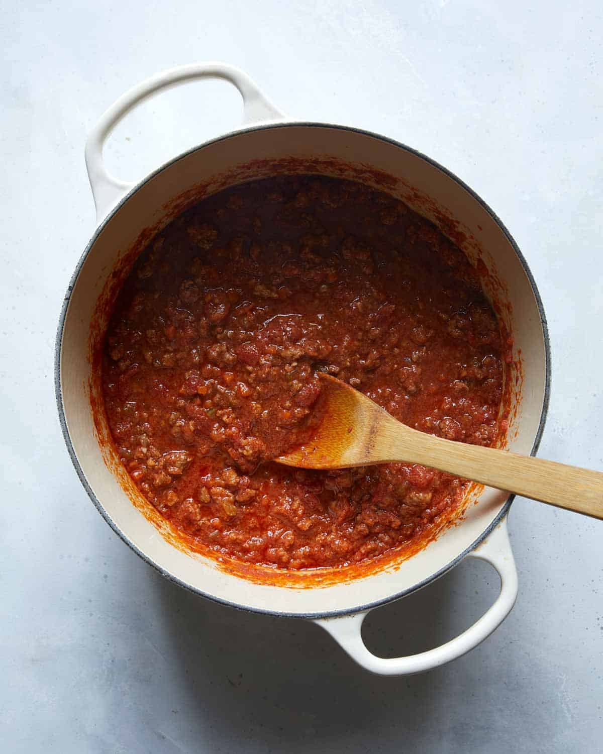 A big pot of bolognese sauce with a wooden spoon in it.