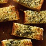 Close up on homemade garlic bread cut into slices on a cutting board.