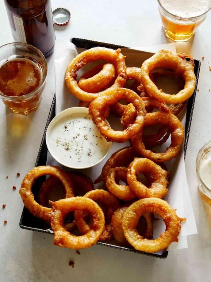Beer battered fried onion rings with beer next to it.