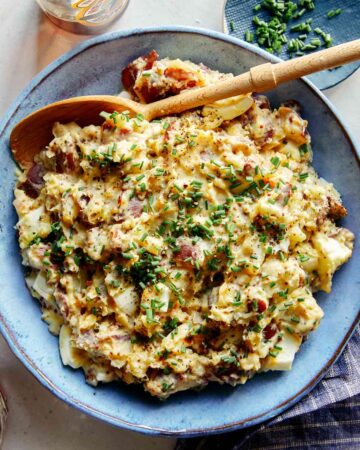 Creamy potato salad in a bowl with a beer on the side.