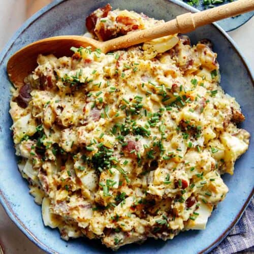 Creamy potato salad in a bowl with a beer on the side.