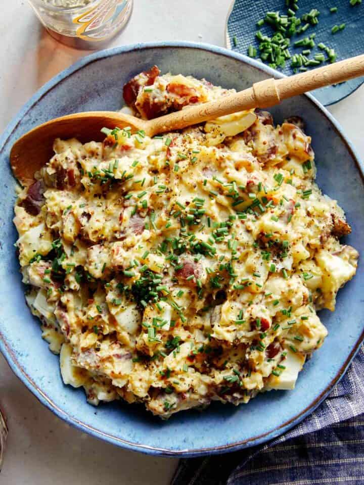 Creamy potato salad in a bowl with a beer on the side.